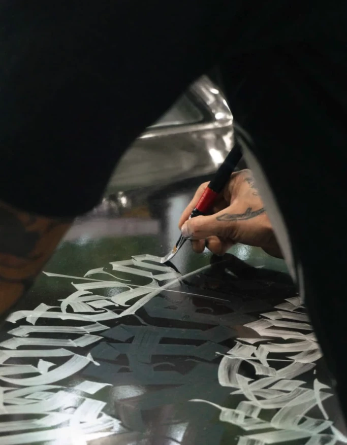 Detalle del pincel dibujando letras blancas sobre una superficie negra